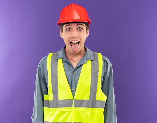 Free photo excited young builder man in uniform showing tongue