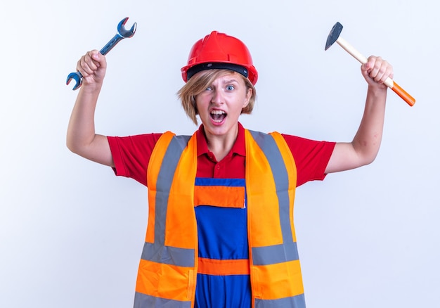 Excited young builder woman in uniform raising open-end wrench isolated on white background