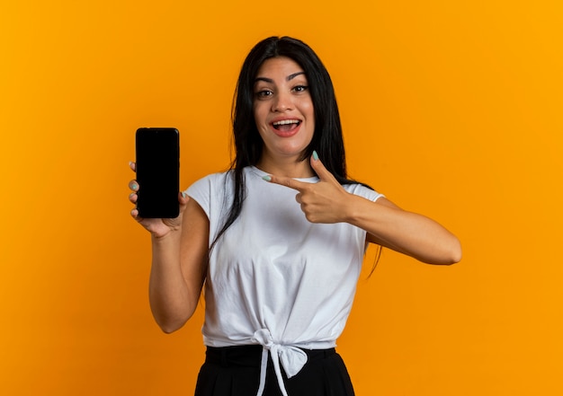 Excited young caucasian girl holds and points at phone 