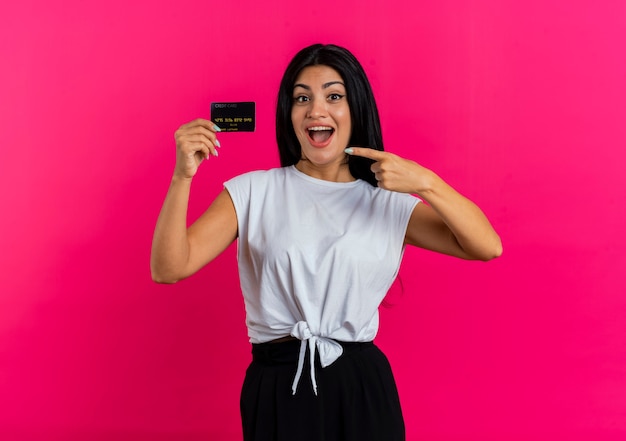 Excited young caucasian woman holds and points at credit card