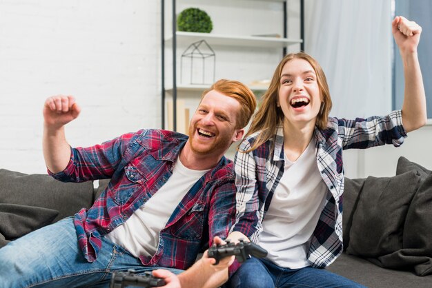 Excited young couple cheering while playing the video game at home