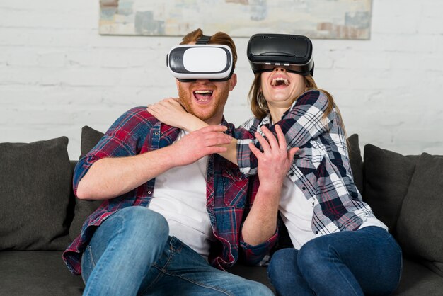 Excited young couple sitting on sofa using a vr headset and experiencing virtual reality