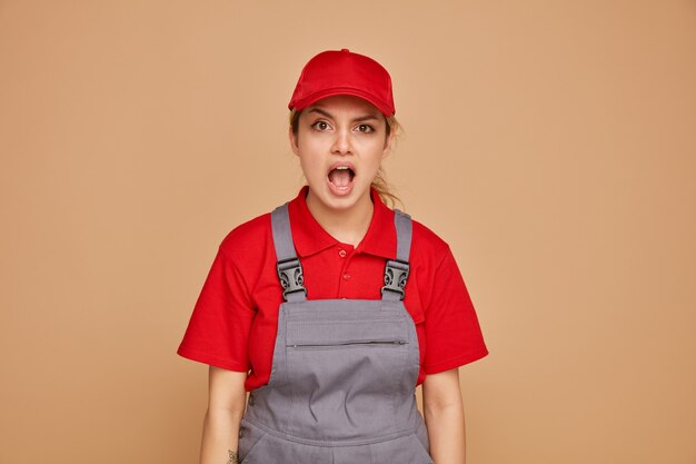 Free photo excited young female construction worker wearing uniform and cap