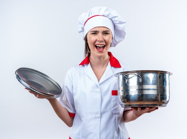 無料写真 白い背景で隔離のふた付き鍋を保持しているシェフの制服を着て興奮した若い女性料理人