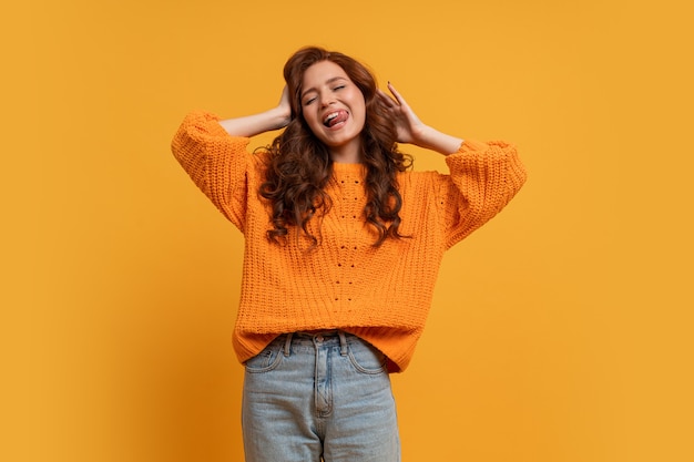 Excited young girl in yellow sweater posing in studio with wavy hair isolated on yellow wall