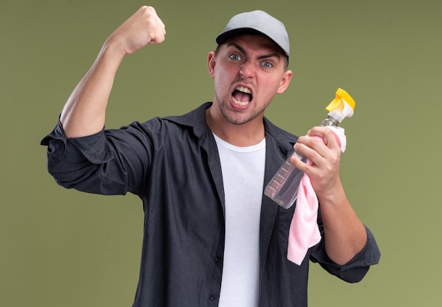 Excited young handsome cleaning guy wearing t-shirt and cap holding rag with spray bottle showing yes gesture isolated on olive green wall