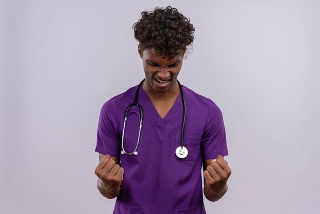 聴診器で握りこぶしで手を上げると紫の制服を着た巻き毛の興奮した若いハンサムな浅黒い医者