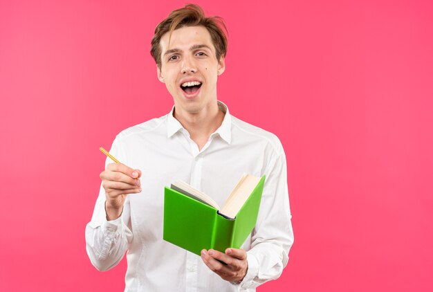 Excited young handsome guy wearing white shirt holding book with pen 