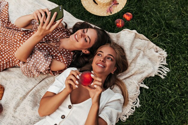 Excited young ladies in summer outfits have picnic on green grass