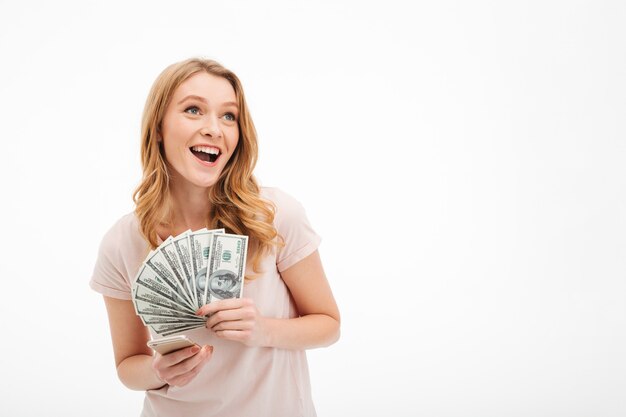 Excited young lady holding money using mobile phone.