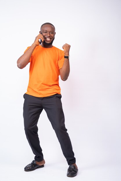 Excited young man celebrates while making phone call isolated on a white wall