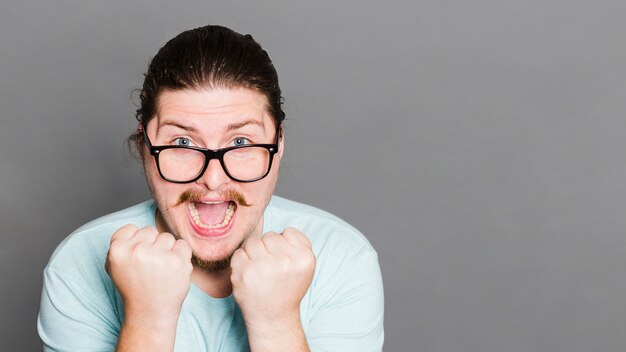 Excited young man flexing his muscle against grey wall