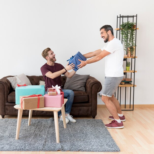 Excited young man giving wrapped gift box to his friend at home