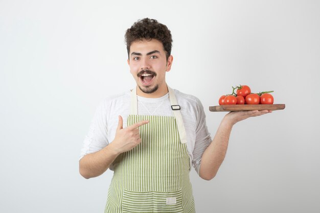 신선한 토마토 더미를 들고 그것에 손가락을 가리키는 흥분된 젊은 남자.