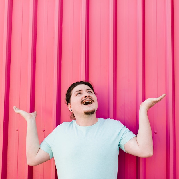 Excited young man looking up shrugging against pink corrugated iron sheet