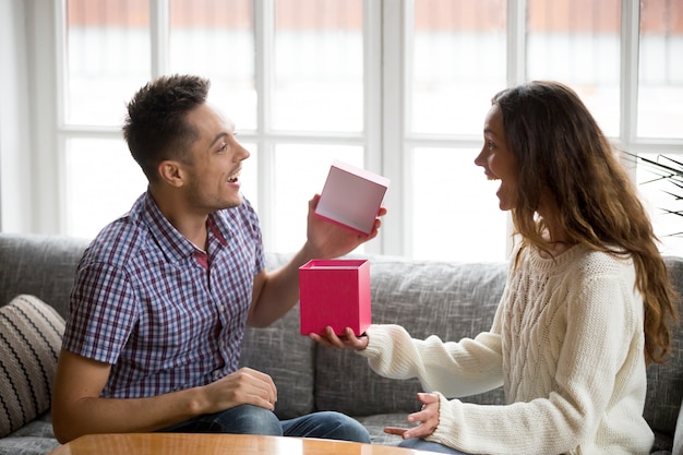 興奮している若い男が妻からプレゼントを受け取るギフトボックスを開く