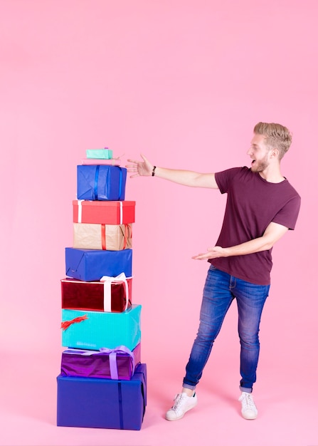 Excited young man showing stack of colorful presents against pink backdrop