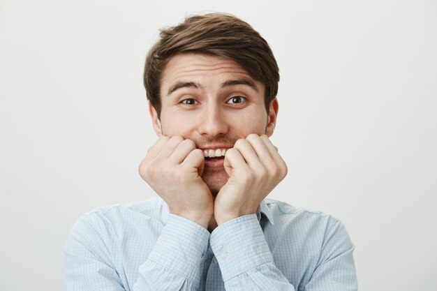 Excited young man smiling, hold hands on face with temptation