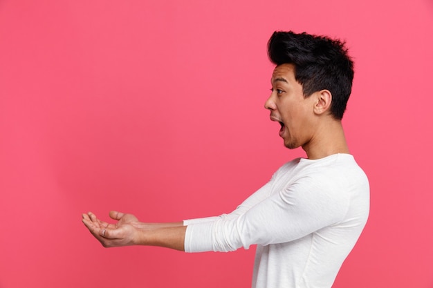 Excited young man standing in profile view looking at side stretching out hands 