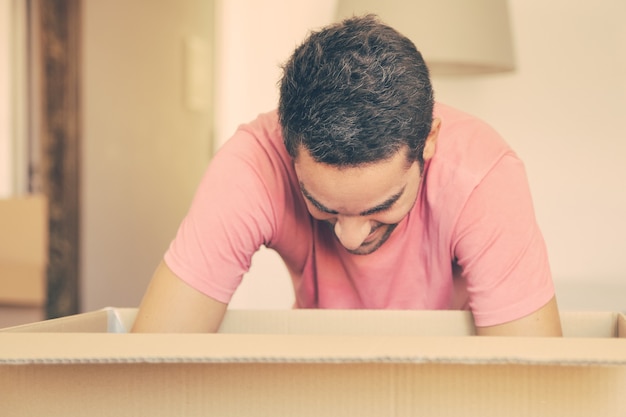 Free photo excited young man unpacking things in his new apartment, opening carton box