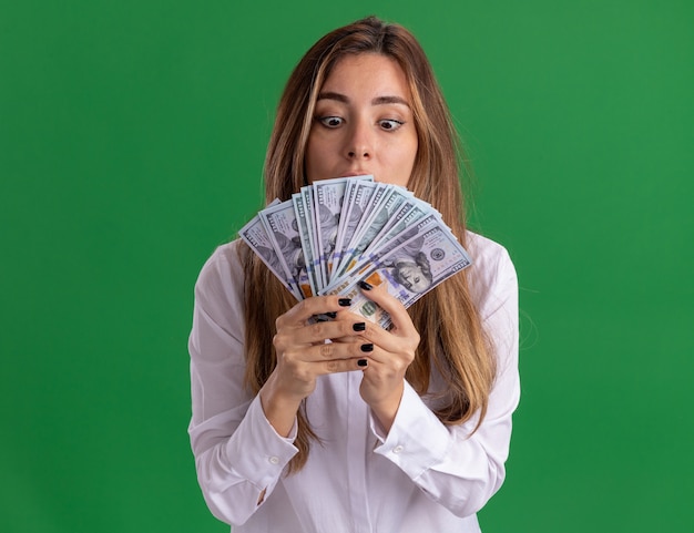 Free photo excited young pretty caucasian girl holds and looks at money isolated on green wall with copy space