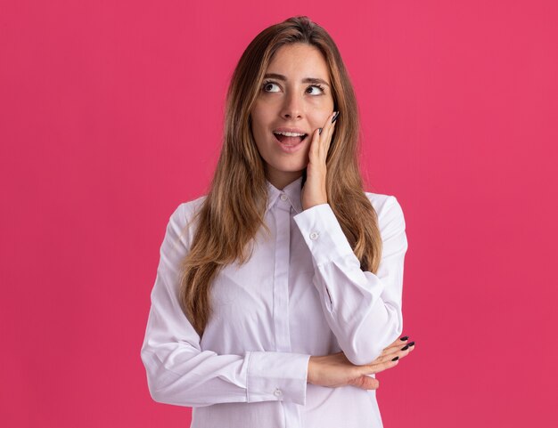 Excited young pretty caucasian girl puts hand on face and looks at side