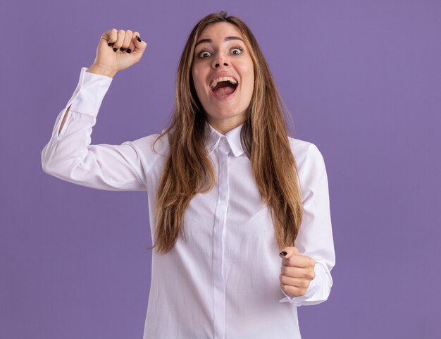 Excited young pretty caucasian girl stands with raised fist on purple 