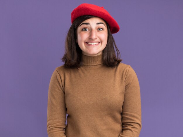 Eccitato giovane ragazza abbastanza caucasica con cappello berretto che guarda l'obbiettivo sulla porpora