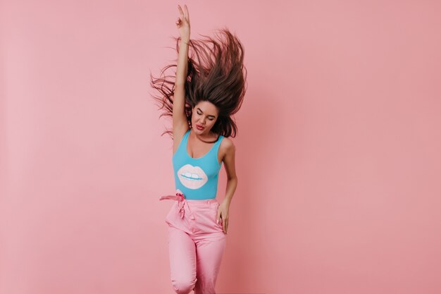 Free photo excited young woman in blue tank-top dancing and laughing with hand up