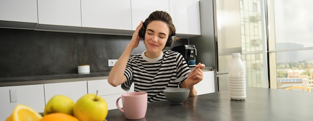 Foto gratuita giovane eccitata che mangia cereali con latte a colazione ascolta musica con le cuffie e