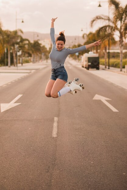 도로에 점프 롤러 스케이트를 입고 평화 서명 몸짓 흥분된 젊은 여성