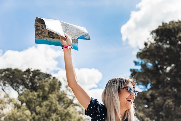 Excited young woman holding map raising her hand