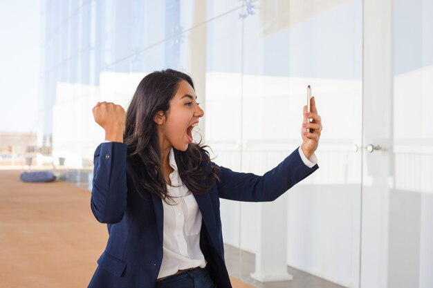 Excited young woman holding smartphone