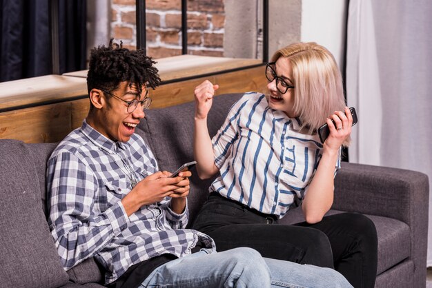 Excited young woman looking at her boyfriend using mobile phone