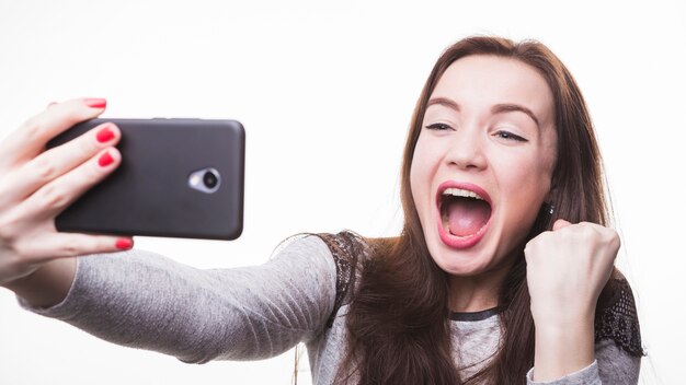 Excited young woman making selfie photo through mobile phone