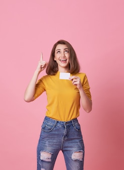 Excited young woman showing credit card and hand point at copy space isolated over pink.