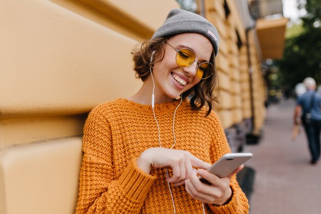 Excited young woman typing message standing near building after walk