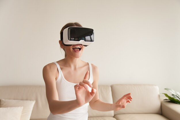 Excited young woman wearing VR headset touching virtual reality