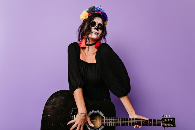 Foto gratuita ragazza emozionante delle zombie che gioca chitarra. meravigliosa donna caucasica in costume nero di halloween divertendosi.