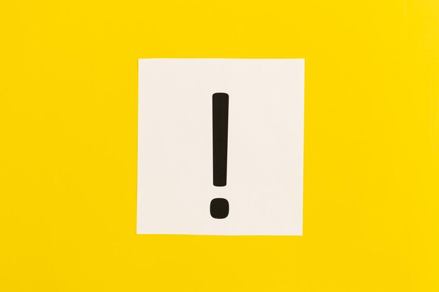 Exclamation mark on white paper on yellow background flat lay