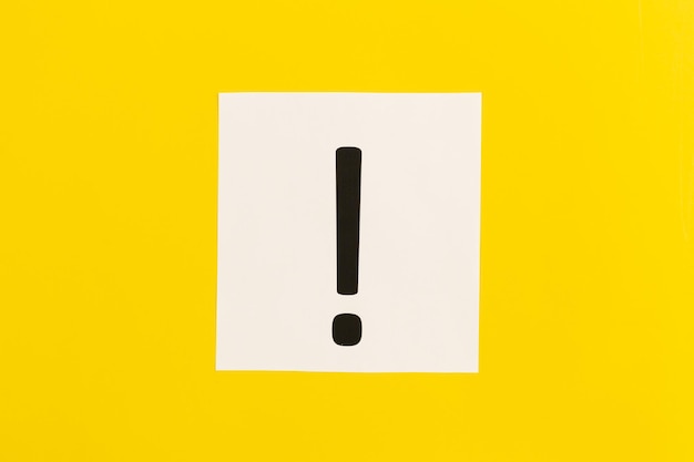 Exclamation mark on white paper on yellow background flat lay