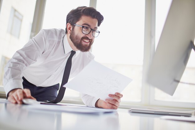 Executive holding a paper and looking at the computer