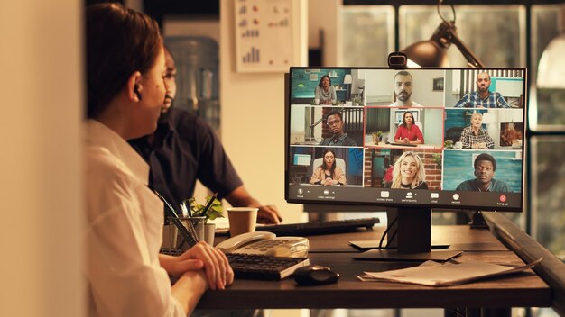 Исполнительный менеджер посещает корпоративную встречу по видеосвязи с веб-камерой в офисе на закате, разговаривает с людьми на удаленной онлайн-конференции. Беседа по соединению видеоконференцсвязи.