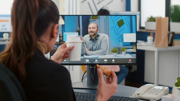 Executive manager eating delivery takeaway pizza during online videocall conference meeting