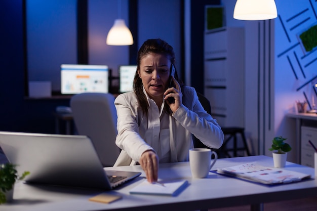 Исполнительный менеджер женщина разговаривает по телефону, проверяя финансовые записи поздно ночью