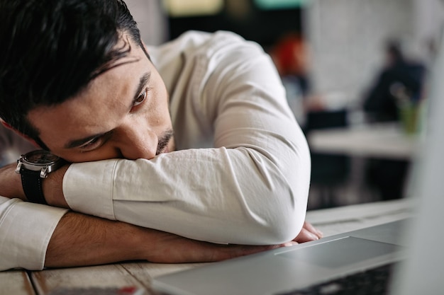 Exhausted businessman leaning on his desk and reading an email on laptop in the office