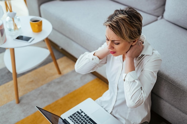 Free photo exhausted businesswoman having a neckache while working on laptop at home