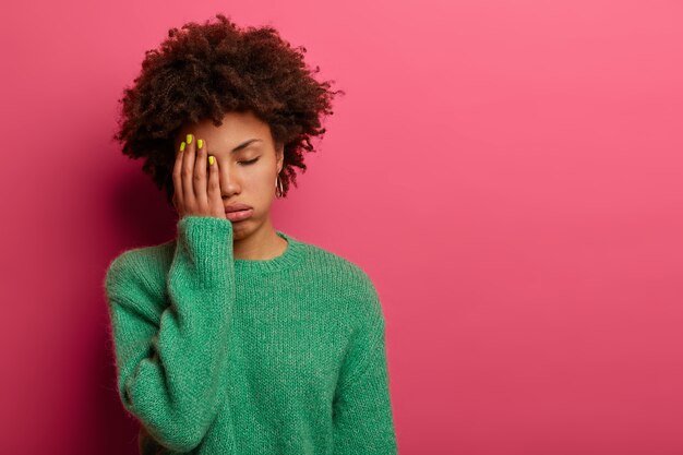 Exhausted dark skinned woman covers half of face, feels tired after working all night