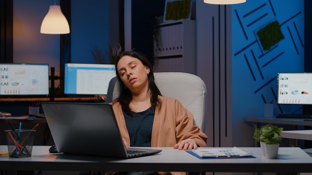 Измученная женщина-предприниматель спит перед ноутбуком во время анализа финансовой статистики