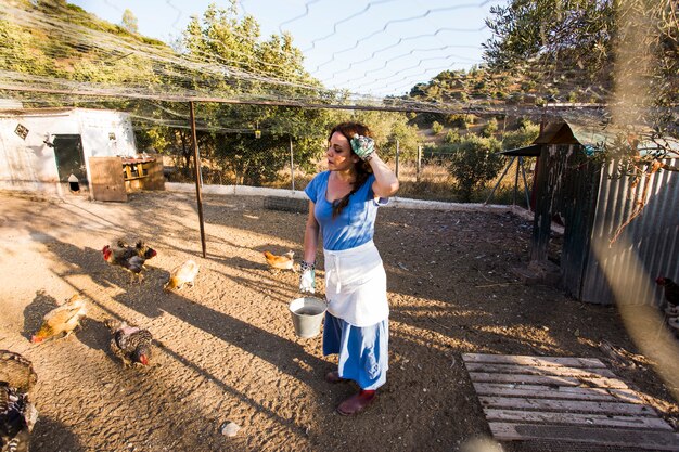 Exhausted female farmer feeding chicken in the field